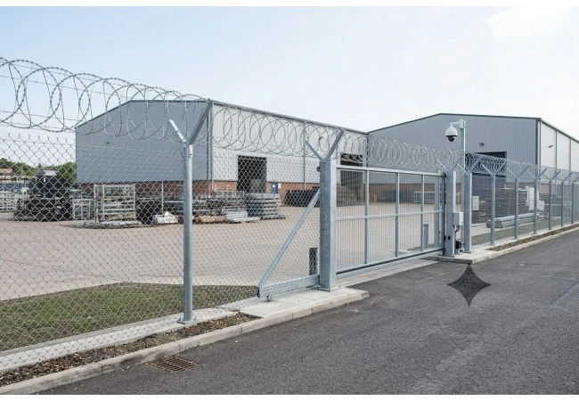 Industrial perimeter survey scene showing fence line posts gate transition and clear access routes affecting razor wire installation labor cost